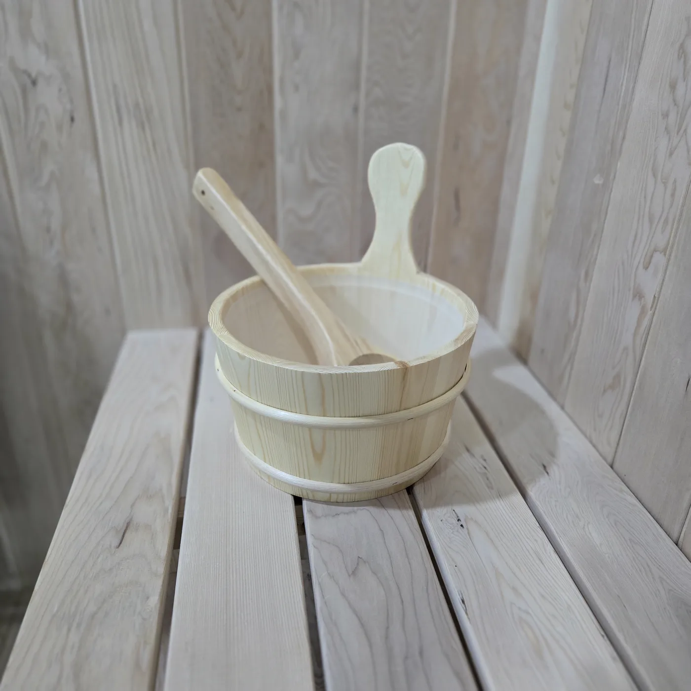 Wooden sauna bucket and ladle mounted on pale timber